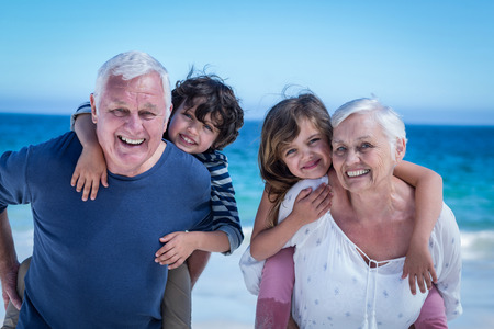 Happy grandparents giving piggy back to children on the beachの写真素材