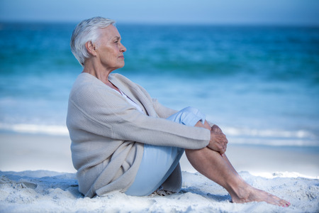 Thoughtful mature woman meditating on the beachの写真素材