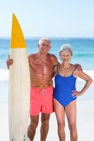 Cute mature couple holding a surfboard on the beachの写真素材