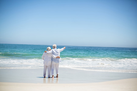 Senior couple embracing and pointing at the beachの写真素材