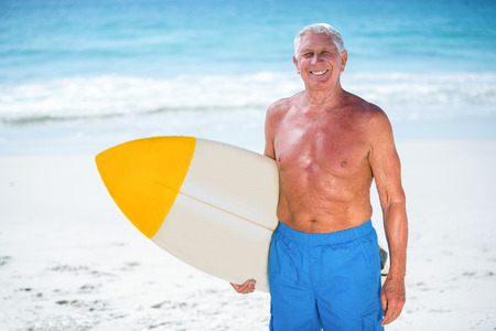 Mature man posing with a surfboard at the beachの写真素材