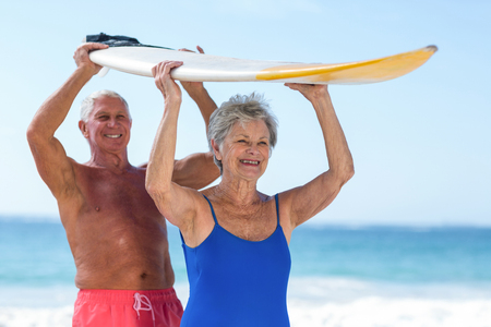 Cute mature couple holding a surfboard over their heads on the beachの写真素材