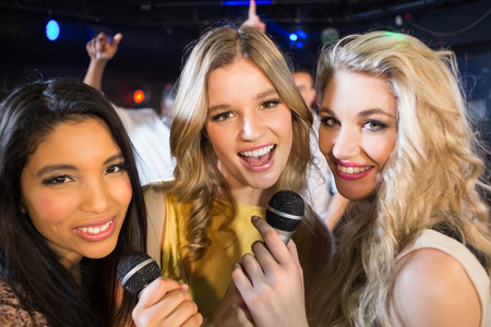 Happy friends singing at the karaoke in night clubの写真素材