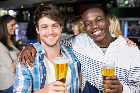 Smiling friends showing beer with their friends in a nightclubの写真素材