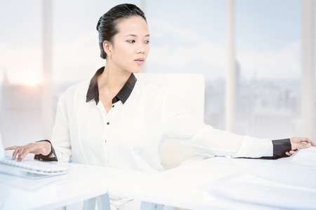 Smiling businesswoman typing on her computer against bright white room with windowsの写真素材