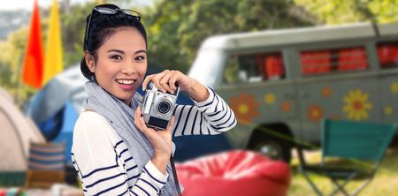 Smiling Asian woman taking photograph with camera against empty campsite at music festivalの写真素材