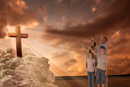 Family of four pointing at copy space against cross religion symbol shape over sunset skyの写真素材