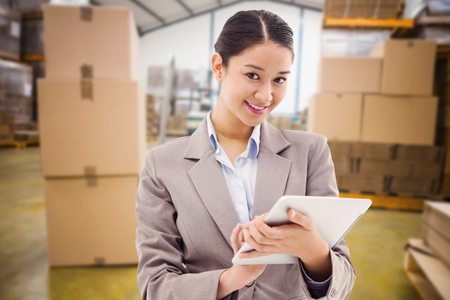 Portrait of a smiling businesswoman using a tablet computer against boxes on trolley in warehouseの写真素材