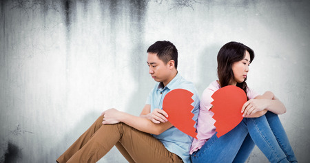 Sad couple holding broken heart pieces against grey backgroundの写真素材