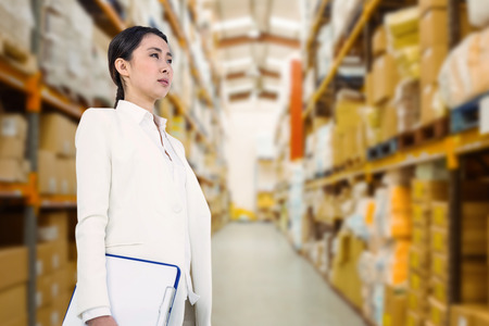 Smiling businesswoman holding clipboard against shelves with boxes in warehouseの写真素材