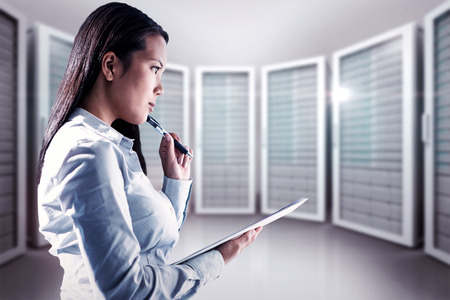 Thoughtful woman with pen on cheek holding notepad against server room