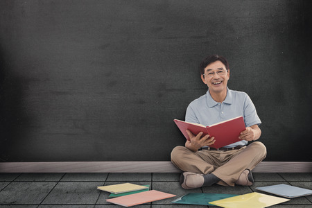 Smiling man reading books against blackboard on wallの写真素材