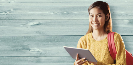 Smiling asian female student using tablet against bleached wooden planks backgroundの写真素材