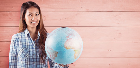 Smiling asian woman holding a globe against overhead of wooden planksの写真素材
