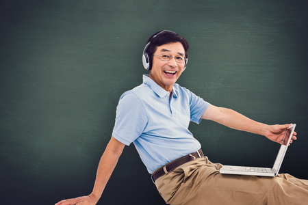 Portrait of cheerful man using laptop while listening music against green chalkboardの写真素材