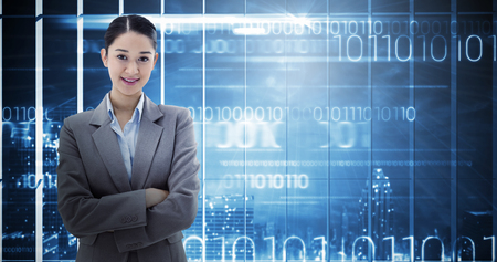 Portrait of a smiling brunette businesswoman posing with the arms crossed against hologram interface in office overlooking cityの写真素材