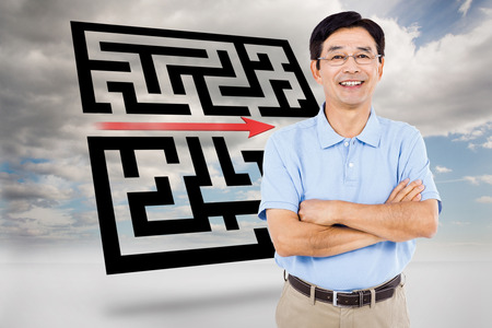 Portrait of happy man with arms crossed against maze with arrow in skyの写真素材