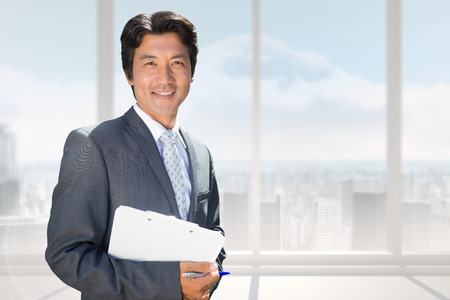 Confident estate agent standing at front door with clipboard against bright white room with windowsの写真素材