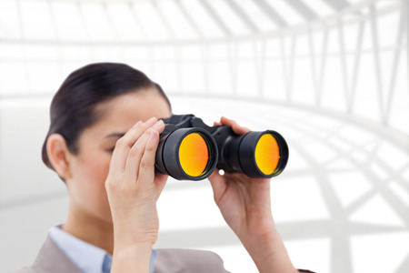 Brunette businesswoman looking through binoculars against spacious roomの写真素材