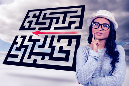 Thoughtful Asian woman standing against maze with arrow in skyの写真素材