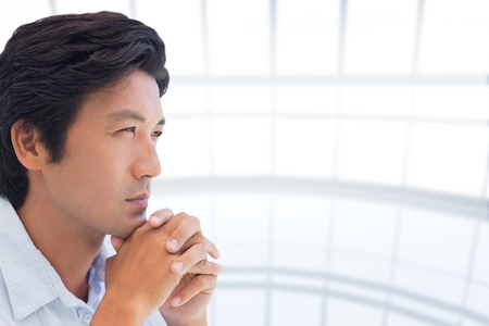Thinking man with hands together against spacious windowsの写真素材