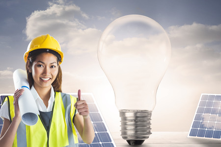 Architect woman with thumbs up against light bulb and solar panels on floorboards in the skyの写真素材