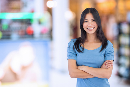 Smiling asian woman with arms crossed against interior of modern shopping mallの写真素材
