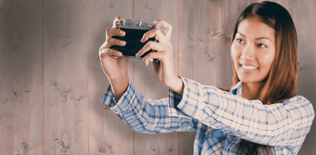 Smiling asian woman taking picture with camera against wooden planksの写真素材