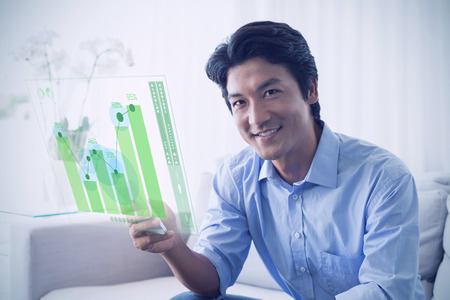 Happy man sitting on couch texting on phone against business interfaceの写真素材