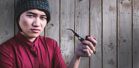 Thoughtful hipster smoking pipe against wooden planksの写真素材