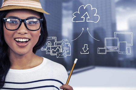 Attractive Asian woman with hat holding pencil against urban sceneの写真素材