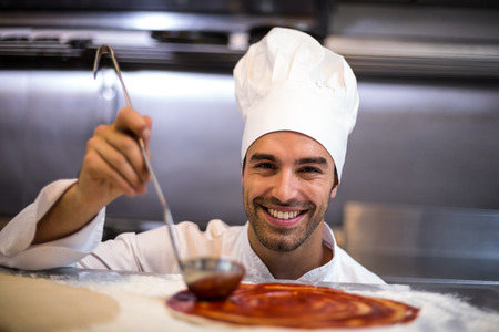 Pizza chef put sauce on base in a commercial kitchenの写真素材