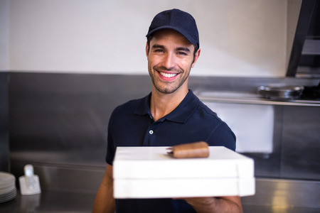 Pizza delivery man showing box in commercial kitchenの写真素材