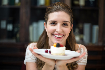 Portrait of happy woman holding desert in plate at restaurant