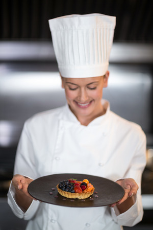 Happy female chef holding plate of dessert in commercial kitchenの写真素材