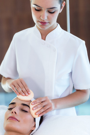 Masseuse cleaning woman face with cotton swabs at spaの写真素材