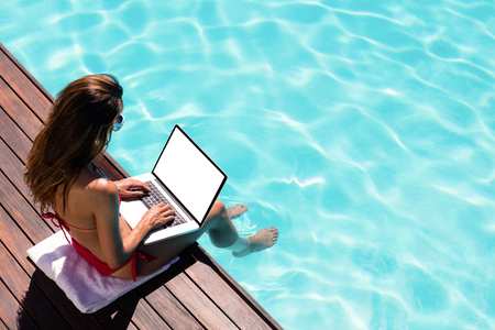 Woman using her laptop on the pool edge on a sunny dayの写真素材