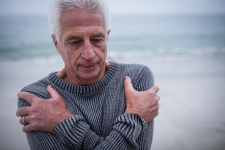 Senior man in sweater feeling cold on beachの写真素材