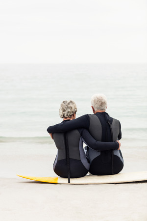 Rear view of couple sitting on surfboard at beachの写真素材