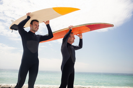 Happy father and son carrying a surfboard over their head on the beachの写真素材