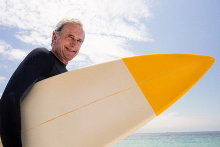 Portrait of senior man in wetsuit holding a surfboardの写真素材
