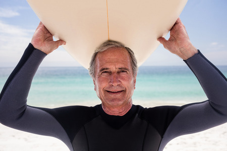 Portrait of senior man holding a surfboard over his head on the beachの写真素材