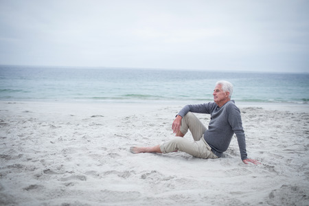Thoughtful retired man sitting on the beach on holidaysの写真素材