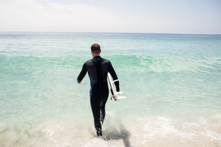 Surfer walking towards sea with a surfboard on a sunny dayの写真素材