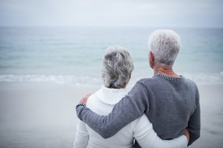 Rear view of senior couple embracing on beach on a sunny dayの写真素材