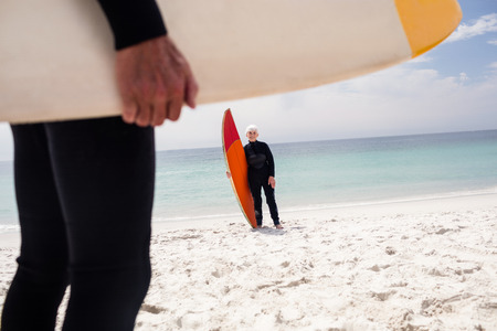 Senior woman in wetsuit holding surfboard on beach on a sunny dayの写真素材