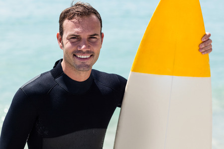 Portrait of happy surfer holding a surfboard on the beach on a sunny day