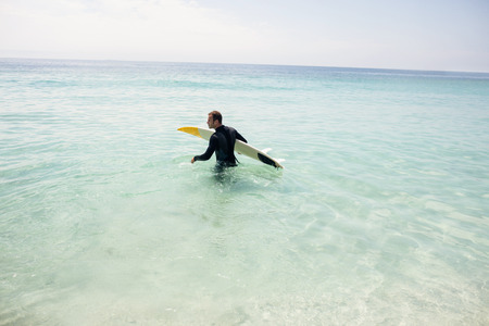 Surfer walking towards sea with a surfboard on a sunny day