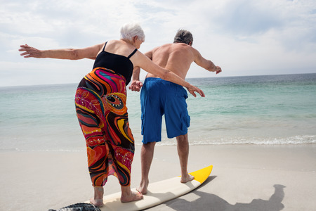 Rear view of senior couple surfing on surfboard on a sunny dayの写真素材