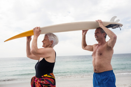 Senior couple carrying a surfboard over their head on beachの写真素材